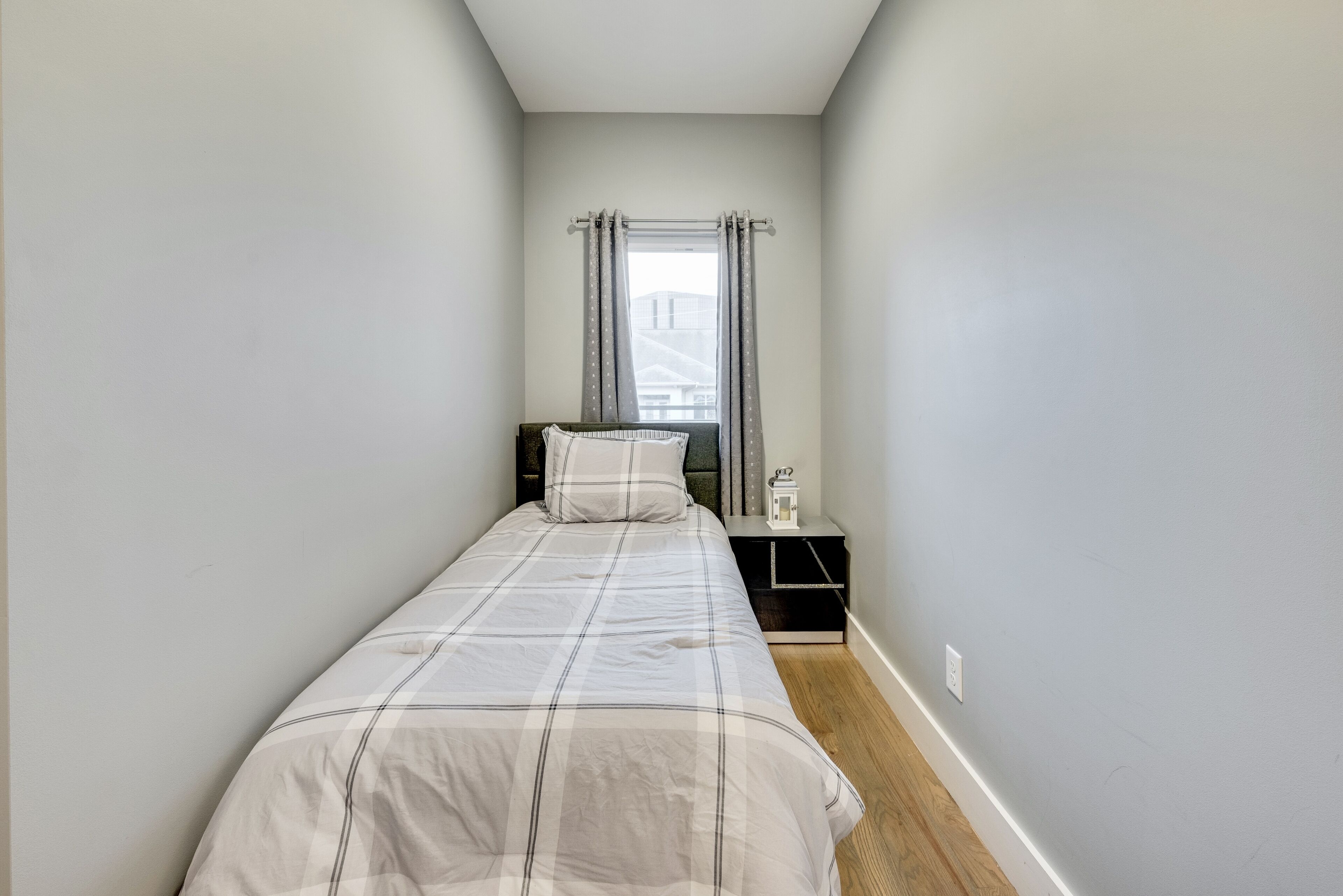 Una habitación pequeña con cama individual, una mesita de noche y una ventana con cortinas.
