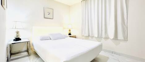 Une chambre d’hôtel avec un grand lit, deux tables de chevet, une commode, un tableau encadré au mur et une fenêtre avec des rideaux.
