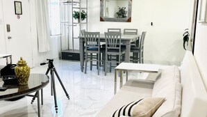 Een moderne woonkamer met een witte bank, een eettafel met stoelen, een plafondventilator en een grote spiegel aan de muur.