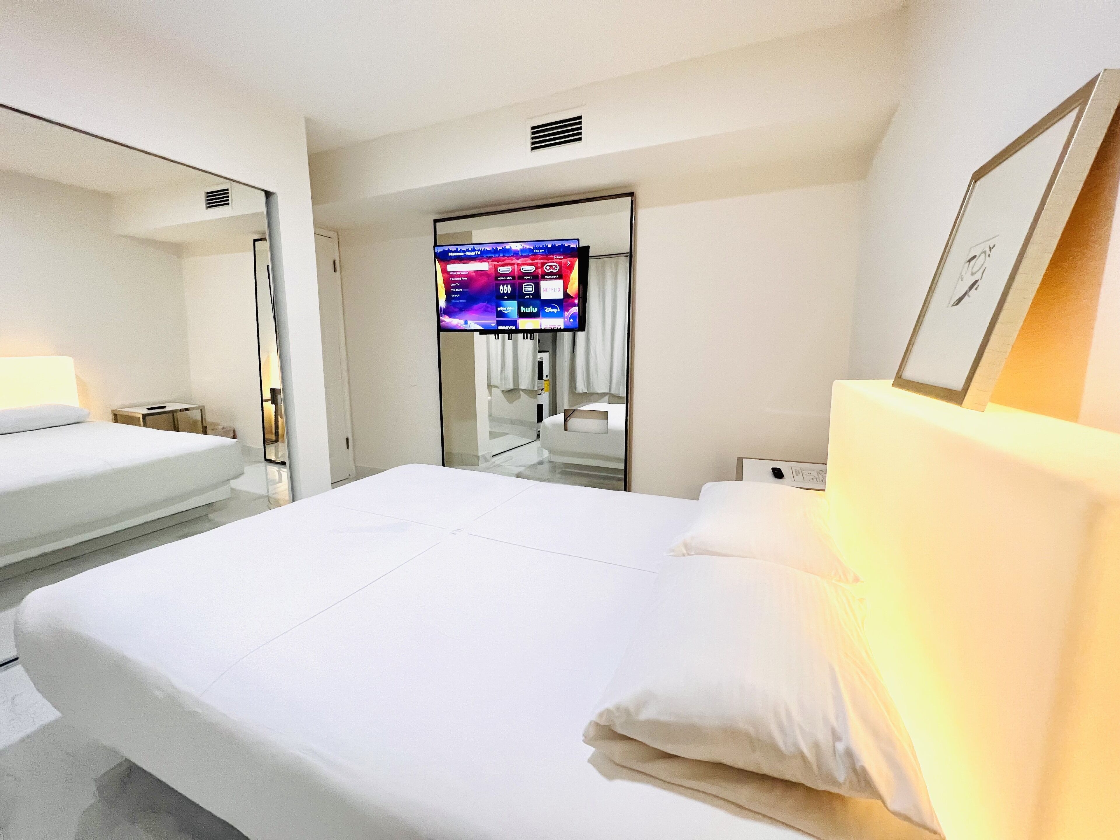 Ein Hotelzimmer mit einem großen Bett, einem an der Wand montierten Fernseher und einem Nachttisch.