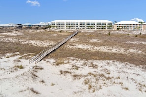 A hotel with multiple floors, a long bridge connecting to the beach, and a sandy landscape.