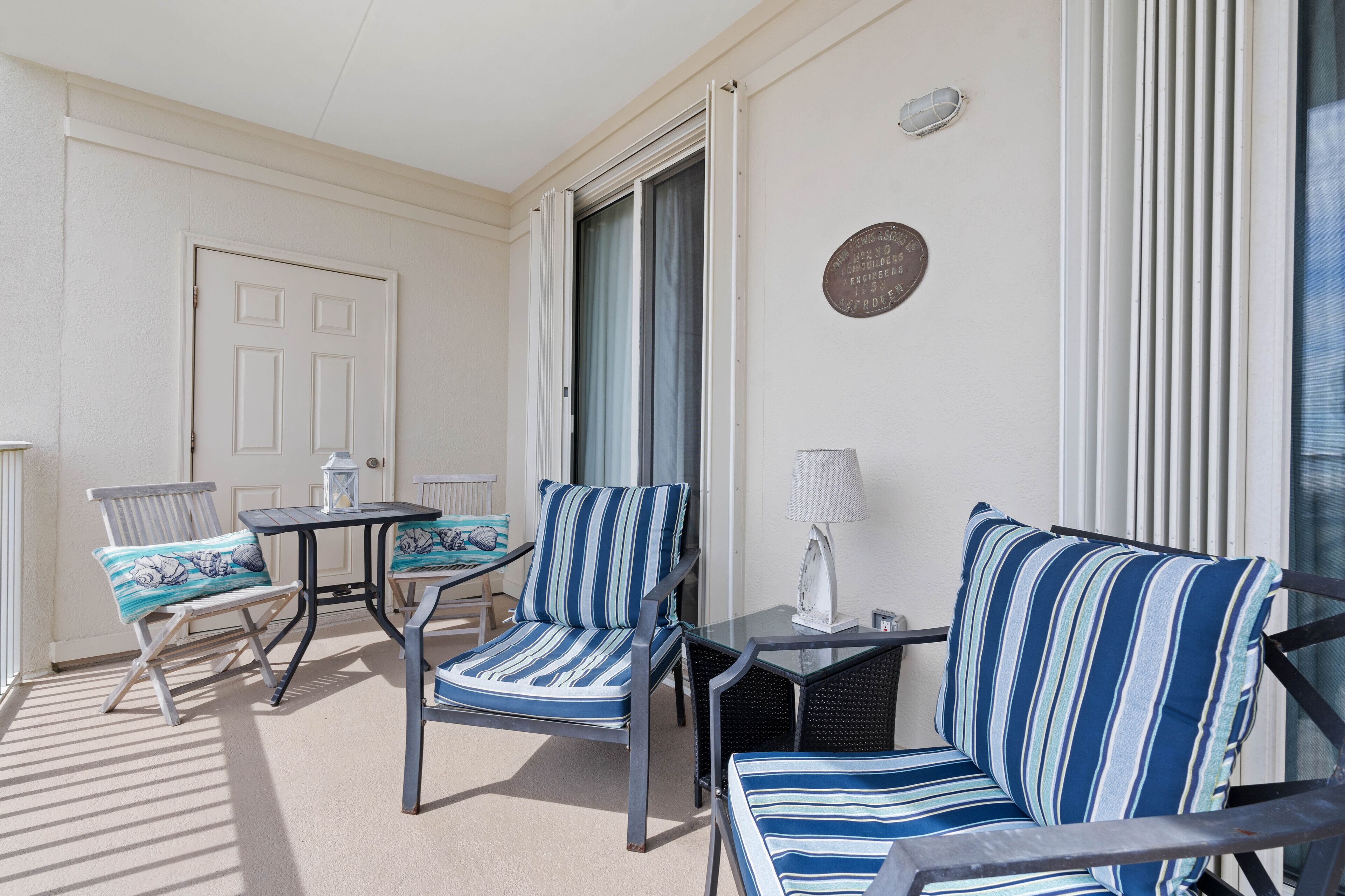 Un espace extérieur lumineux, aménagé avec des chaises à rayures et un canapé, une table et une porte donnant sur l’intérieur.