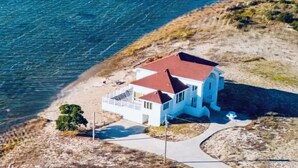 An aerial view of a coastal house with a red roof, white walls, and a balcony overlooking the sea. - SOUND FRONT / Kite-in/out Direct Beachfront Access Sunsets Best Kiteboard Spot (Rodanthe)
