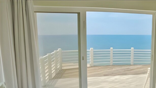 A bedroom with a large bed, white curtains, and a view of the ocean through a sliding glass door. - SOUND FRONT / Kite-in/out Direct Beachfront Access Sunsets Best Kiteboard Spot (Rodanthe)