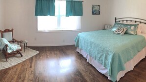 Une chambre à coucher avec un lit, une chaise, une fenêtre avec des rideaux et une petite table.