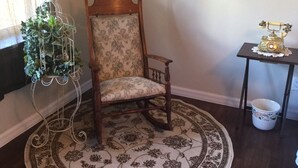 Une chaise en bois avec un coussin à motifs floraux, un présentoir en métal décoratif avec une plante, et un téléphone ancien posé sur une petite table.