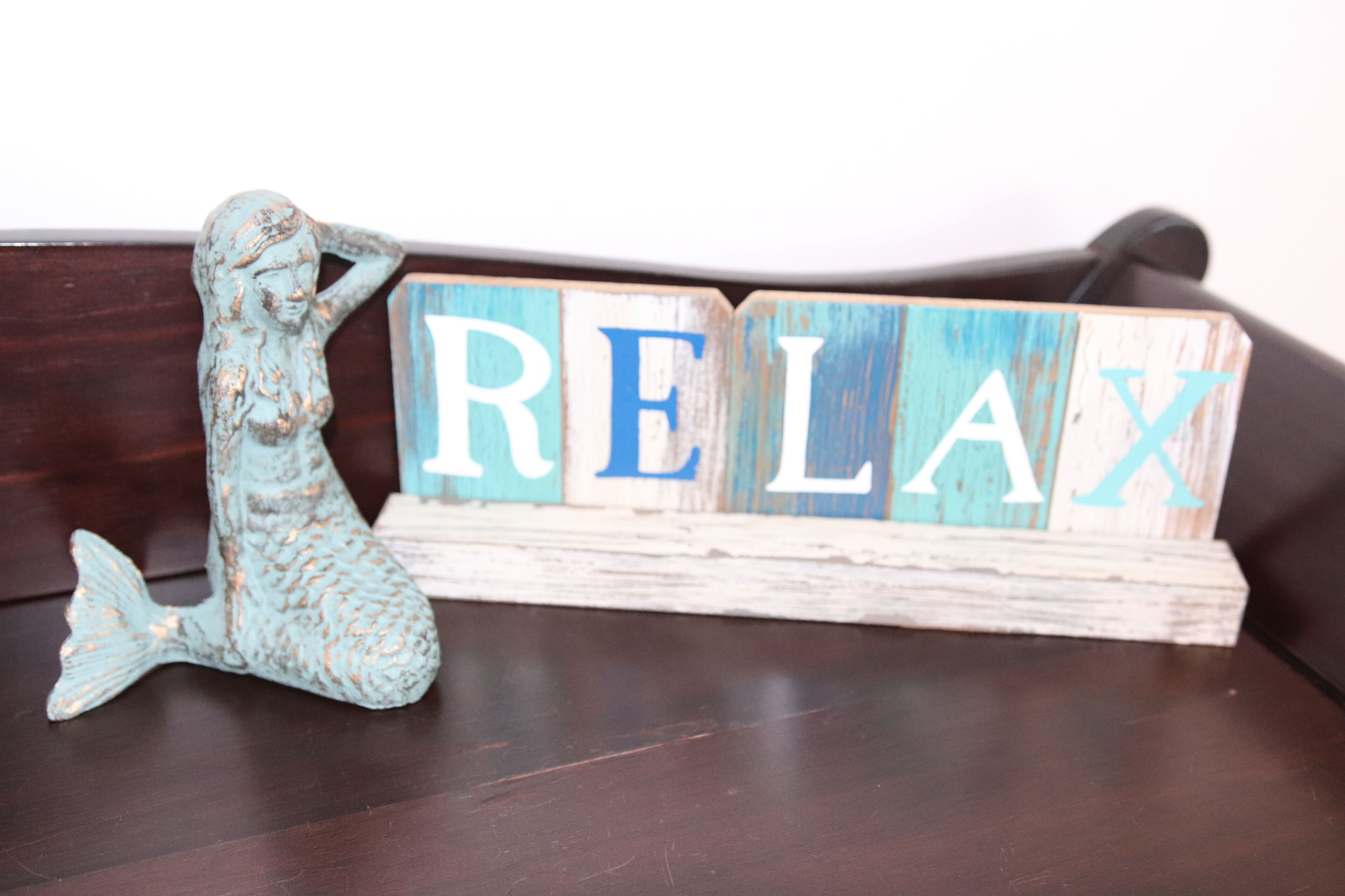 Koristeellinen puupala, jossa on sana ”RELAX” ja pieni merenneitohahmo.