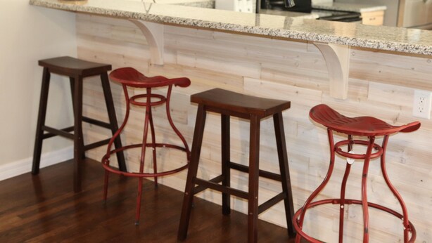 Une cuisine dotée d’un comptoir en granit, de meubles en bois et d’un réfrigérateur en acier inoxydable. On y trouve trois tabourets de bar rouges avec des pieds en métal.