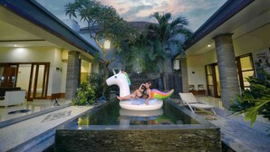 A pool area with a unicorn float, lounge chairs, and tropical plants. - Krishna Villas (Legian)
