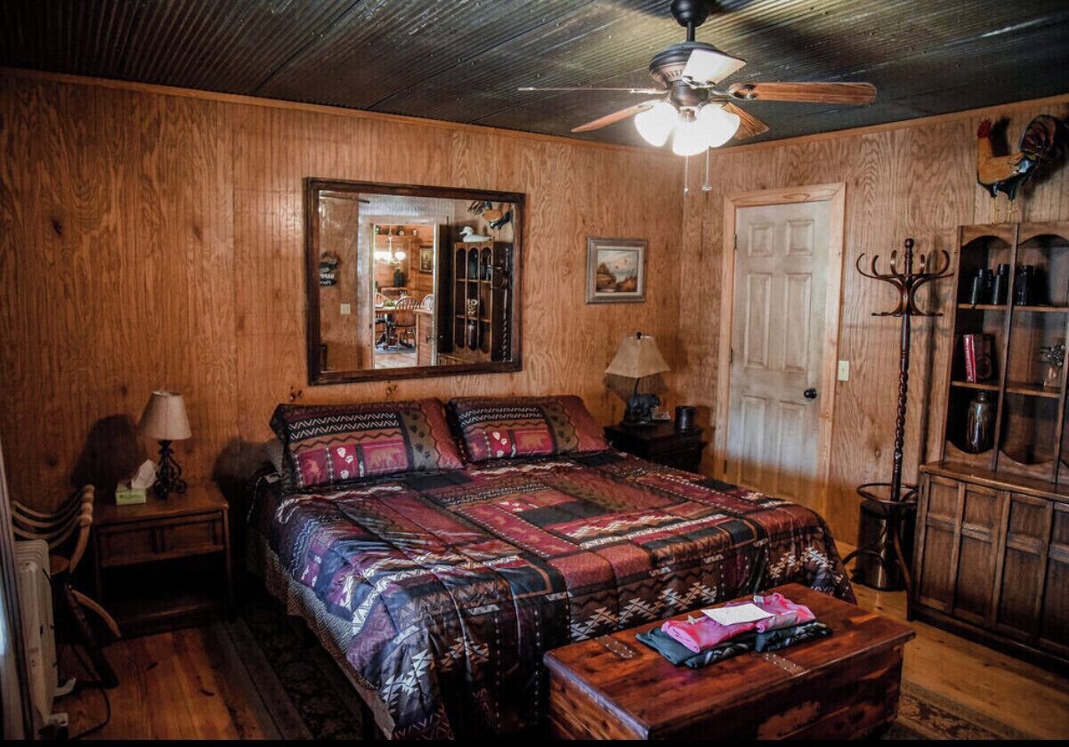 A cozy bedroom with a large bed, wooden walls, a ceiling fan, and a wooden cabinet with glass doors.