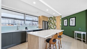 A modern kitchen with a large island, wooden chairs, a refrigerator, and a green accent wall with artwork.