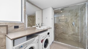 A modern bathroom with a large mirror, a sink, a shower, and a built-in washing machine.