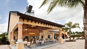 Eine Terrasse im Freien mit Tischen und Stühlen, einem überdachten Sitzbereich und Palmen.