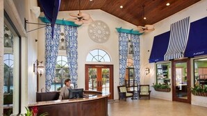 Eine Hotelhalle mit einer Rezeption, großen Fenstern und Deckenventilatoren.