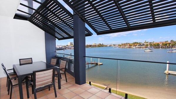 Een balkon met een tafel en stoelen, met uitzicht op een jachthaven met boten en gebouwen op de achtergrond.