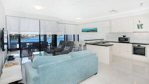 Un salon moderne comprenant un canapé, un coin repas et une cuisine avec des meubles et des appareils électroménagers blancs.