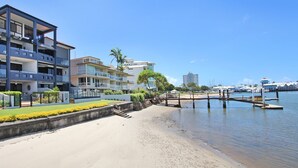 Un hôtel situé en bord de mer, doté de nombreux balcons, d’une plage de sable et d’un port de plaisance avec des bateaux.