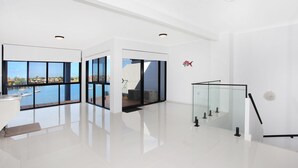 Un intérieur spacieux et moderne, doté de grandes fenêtres offrant une vue sur un port de plaisance et des immeubles.