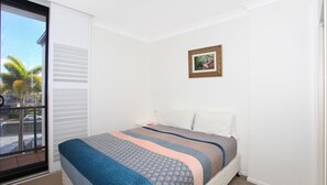 A bedroom with a bed, a nightstand, a window with blinds, and a framed picture on the wall. - Kirribilli 13 - Two Bedroom Apartment with River View! (Mooloolaba)