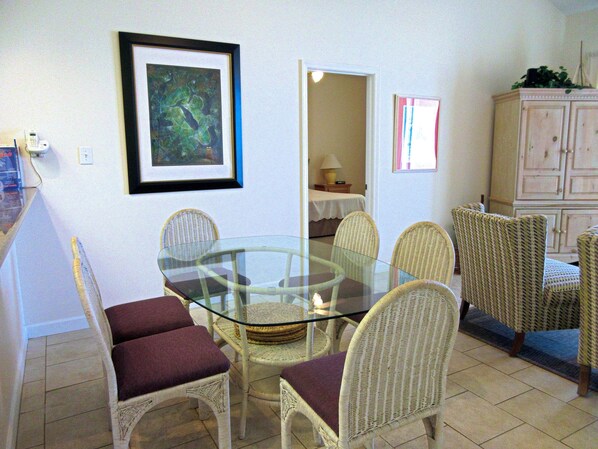 A dining area with a glass table surrounded by wicker chairs with cushioned seats.