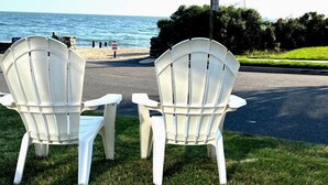 Kaksi valkoista muovista Adirondack-tyylistä tuolia, jotka on asetettu vastakkain rantaa kohti, ja taustalla näkyy valtameri.