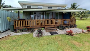 A single-story house with a wooden deck, a small porch, and a grassy yard. - Capture the view, hear the waves -TepaeruVista (Vaimaanga)