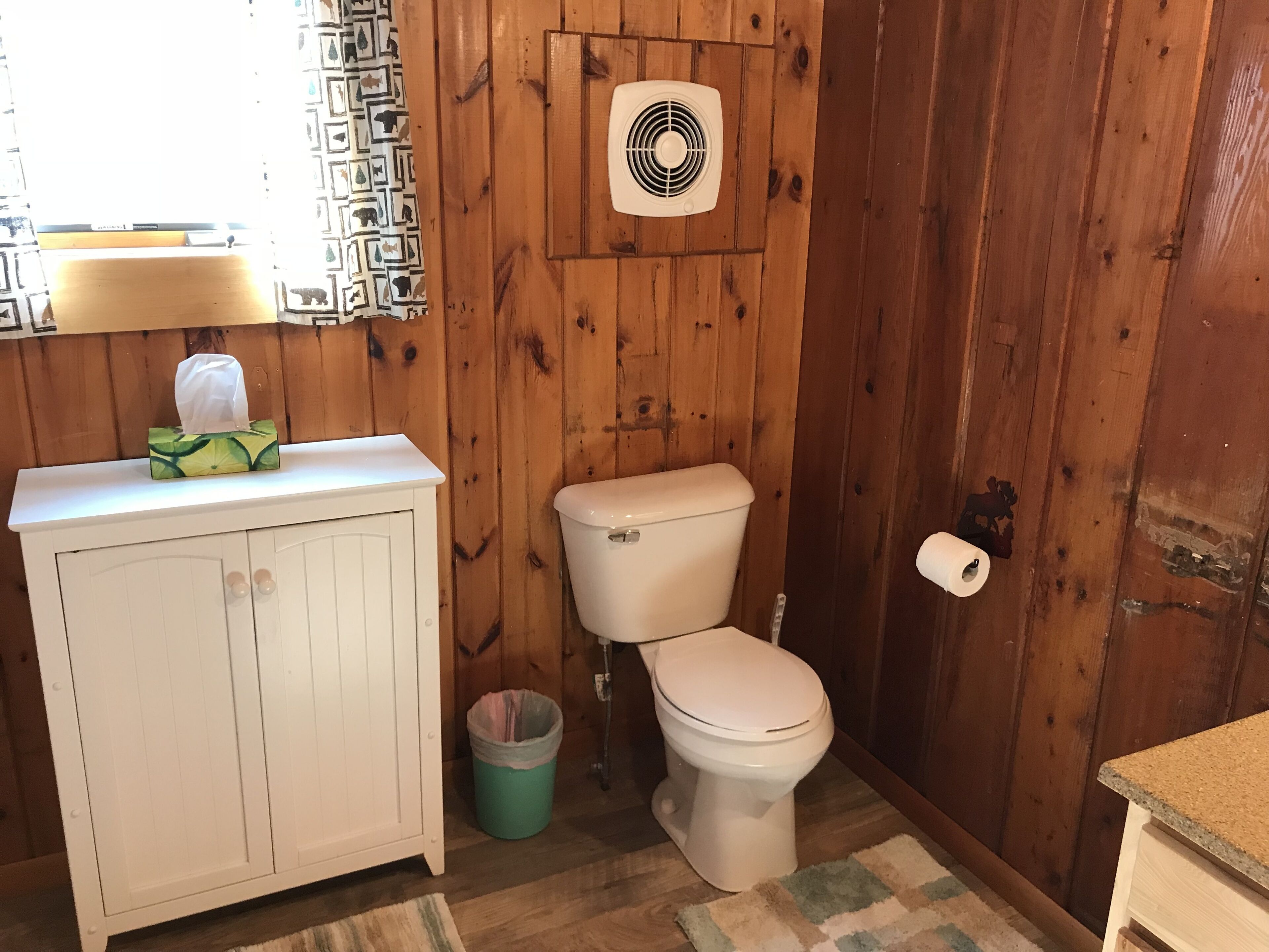 A small bathroom with a wooden wall, a toilet, a sink, and a trash can.
