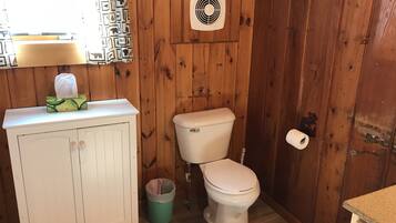 A small bathroom with a wooden wall, a toilet, a sink, and a trash can.