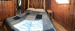 Una habitación de madera con una cama, una mesita de noche y una puerta de madera.