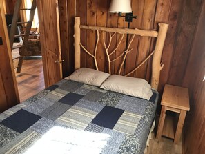Une pièce en bois avec un lit, une table de chevet, une échelle et une lampe.