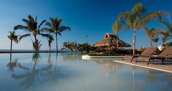 A poolside area with lounge chairs, palm trees, and a thatched-roof structure.