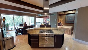 Una cocina moderna con una isla central, un comedor con sillas y vistas al exterior.