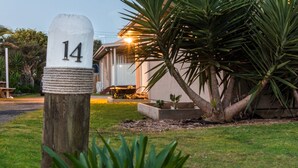 Un poste de madera con un letrero blanco que muestra el número 14, una casa con porche y una planta grande al frente.