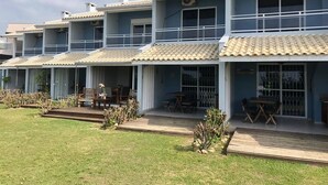 A row of blue buildings with tiled roofs, outdoor seating areas, and a grassy lawn. - 3 SEA-FRONTED Houses - Beach of Mariscal, Bombinhas, SC - HOUSE #2 (Canto Grande)