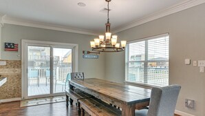 Uma sala de jantar com mesa e bancos de madeira, um candelabro e vista através de uma porta de correr de vidro.