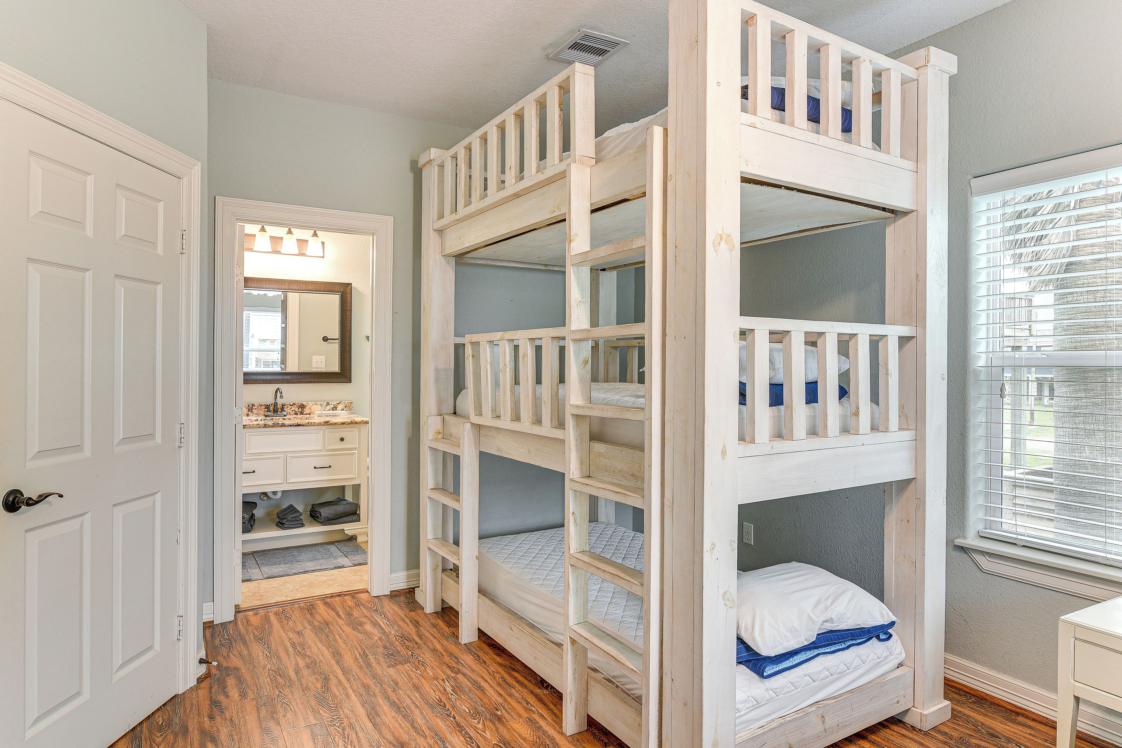 A room with a bunk bed, a bathroom with a vanity, and a window with blinds.