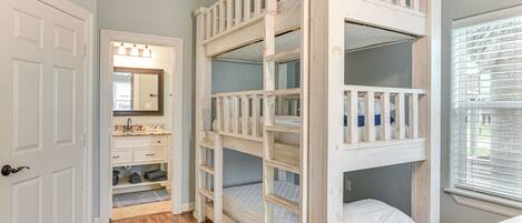 A room with a bunk bed, a bathroom with a vanity, and a window with blinds.