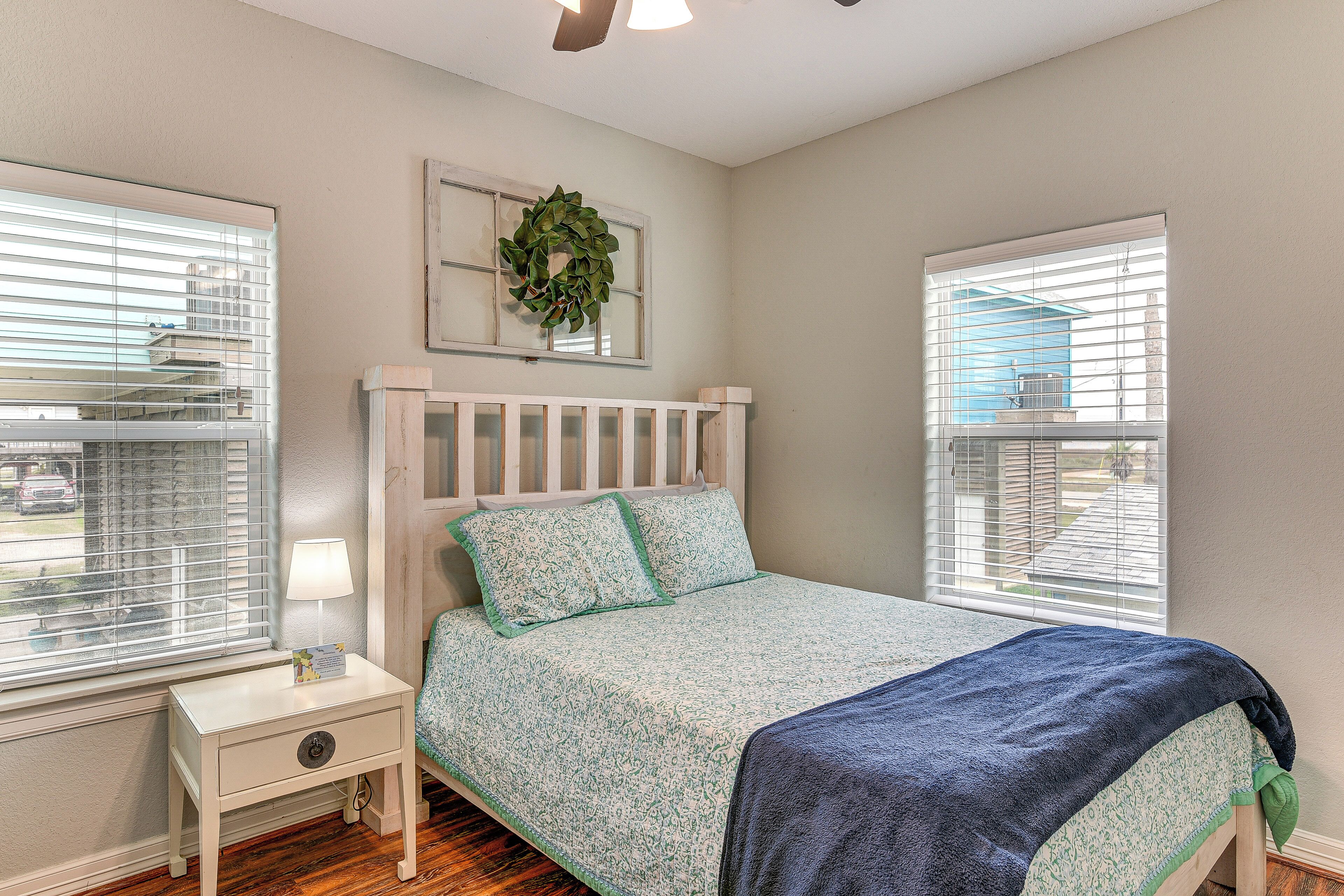 A bedroom with a bed, nightstand, and two windows with blinds.