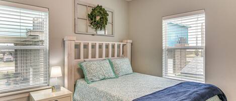A bedroom with a bed, nightstand, and two windows with blinds.