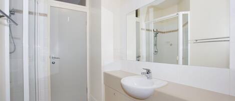 A bathroom with a white sink, a mirror, and a shower enclosure.
