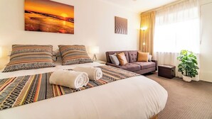Une chambre d’hôtel avec un lit, un canapé, un tableau, une lampe, une plante et une fenêtre avec des rideaux.