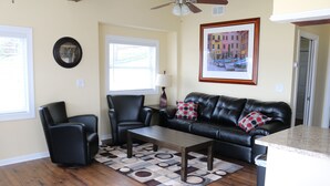 A living room with a black leather sofa, two black armchairs, a wooden coffee table, and a patterned rug.