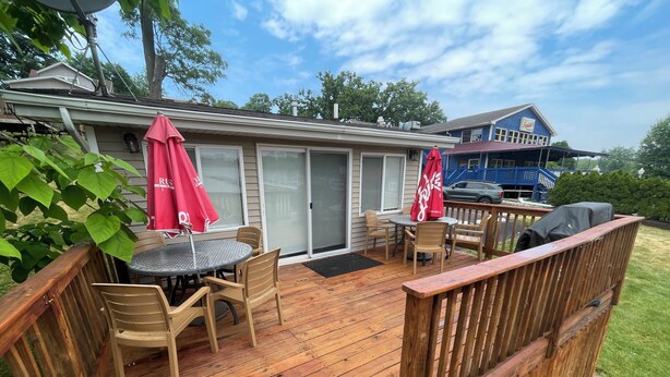 A wooden deck with a table and chairs, a barbecue grill, and a covered patio area with umbrellas.