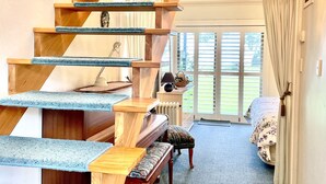 Eine Holztreppe mit blauem Teppich führt zu einem Wohnbereich mit einem Klavier, einer Bank und einem Sofa.
