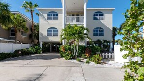 A two-story building with a balcony on the second floor, surrounded by palm trees and a white fence.