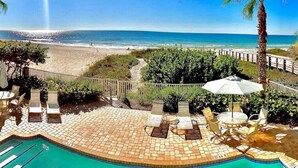 A pool area with lounge chairs and umbrellas, a wooden deck, and a view of the beach and ocean.