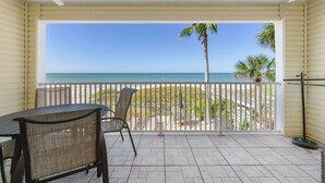 A covered balcony with a view of the ocean, a table, chairs, and a ceiling fan.