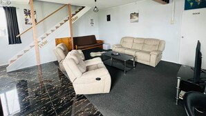 A living room with a sofa, armchair, and coffee table. There is a staircase with a 'Relax' sign, a bookshelf with books, and a world map on the wall. - Our house is the perfect holiday home (Raetihi)
