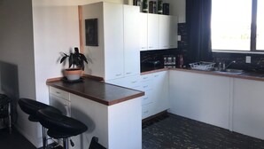 A compact kitchen with white cabinets, a countertop, a sink, and a bar stool. - Our house is the perfect holiday home (Raetihi)