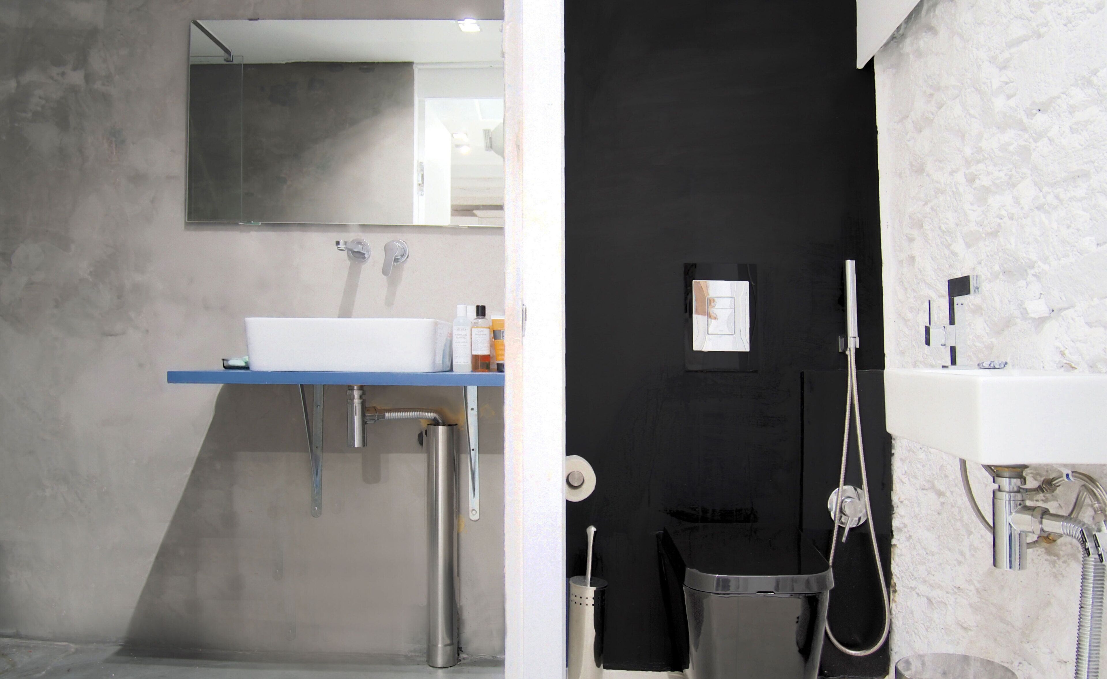 Une salle de bain avec un lavabo blanc, un miroir et un mur noir.